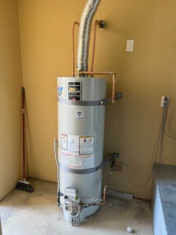 Plumber in blue shirt and overalls, using a wrench on a water heater in a utility room.