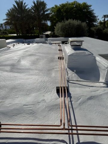 A plumber in a plaid shirt and hat works on white pipes in a basement, wearing gloves.