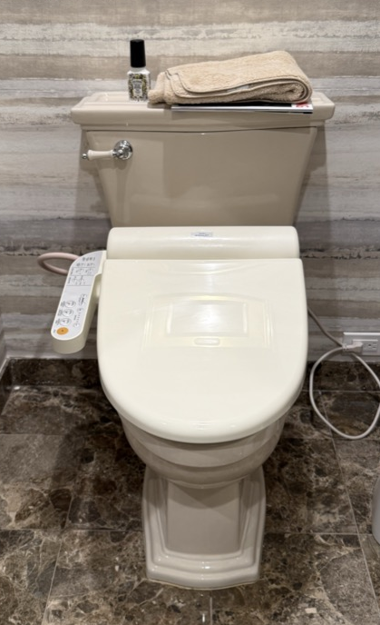 Plumber in blue work clothes, orange gloves, and tool belt, fixing a white sink in a bathroom.