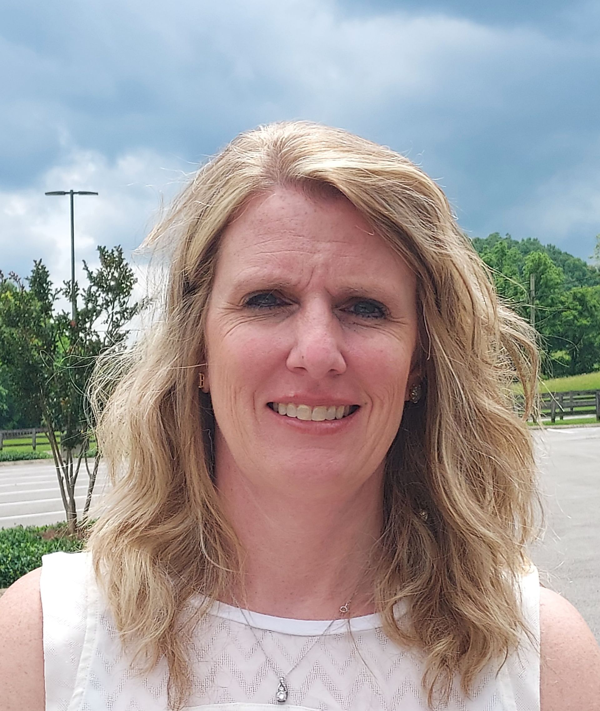 A woman with blonde hair and a white shirt is smiling for the camera.
