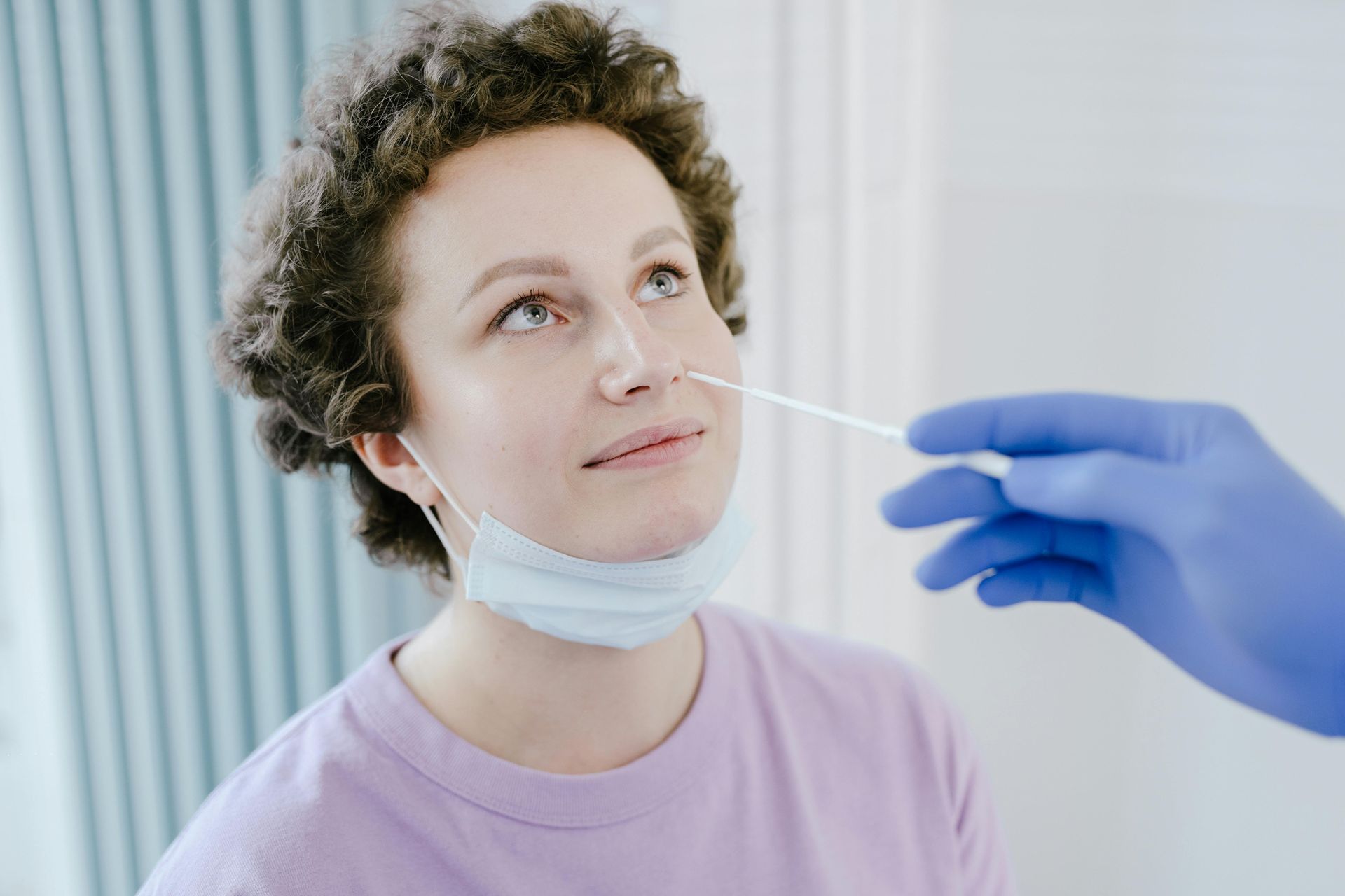 A woman wearing a mask is getting a swab from her nose.