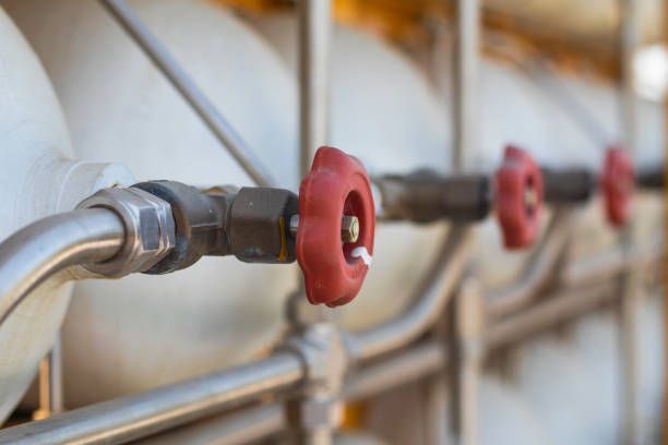 Red handled valves on a row of white cylindrical tanks, connected by silver piping.