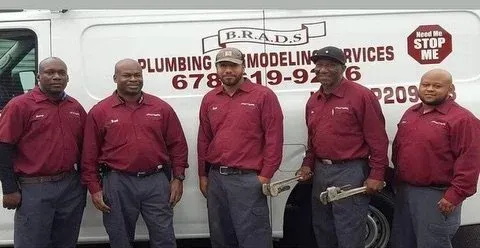 Five men in red shirts and dark pants stand in front of a white van with Five men in red shirts and dark pants stand in front of a white van with