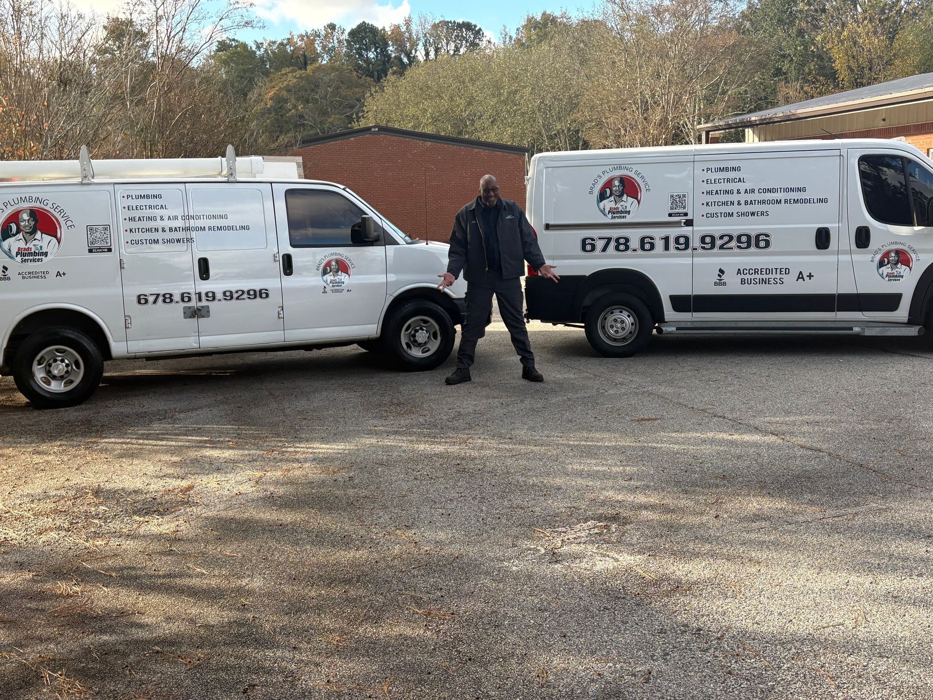 Man standing between two white service vans, parked on gravel.