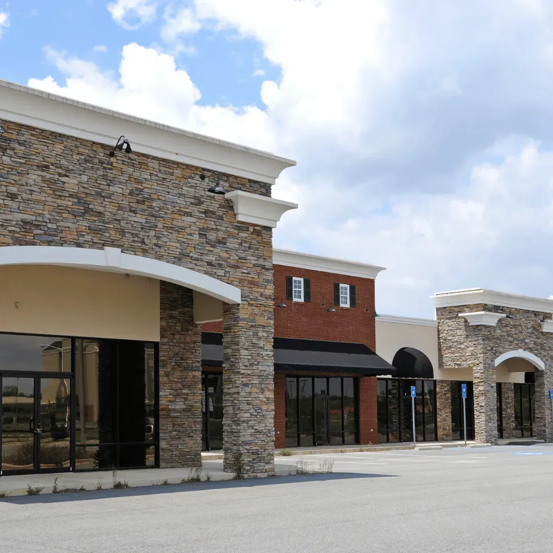 Empty retail storefronts with stone and brick facades under a cloudy sky.