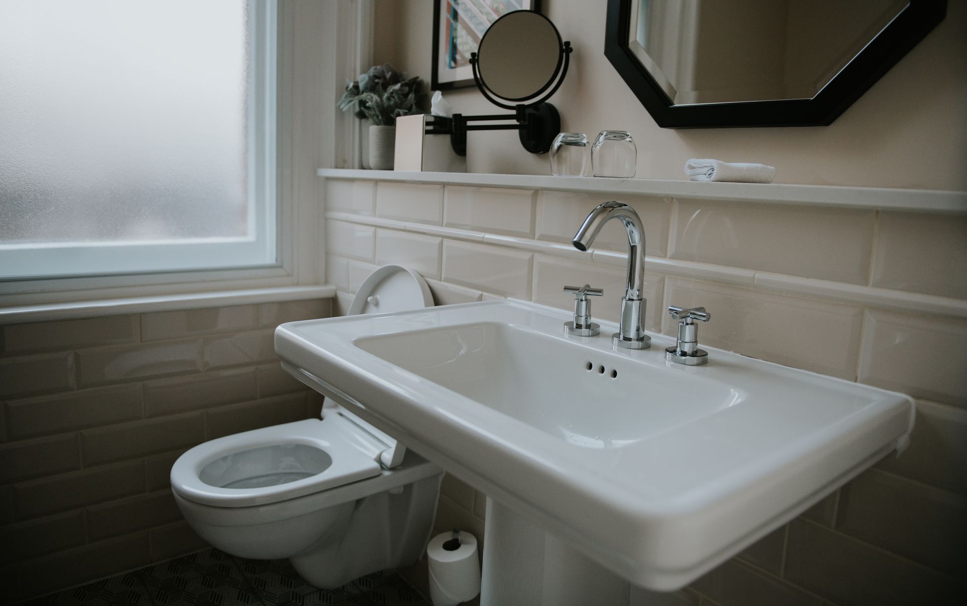 Bathroom with a white pedestal sink, toilet, and window with frosted glass.