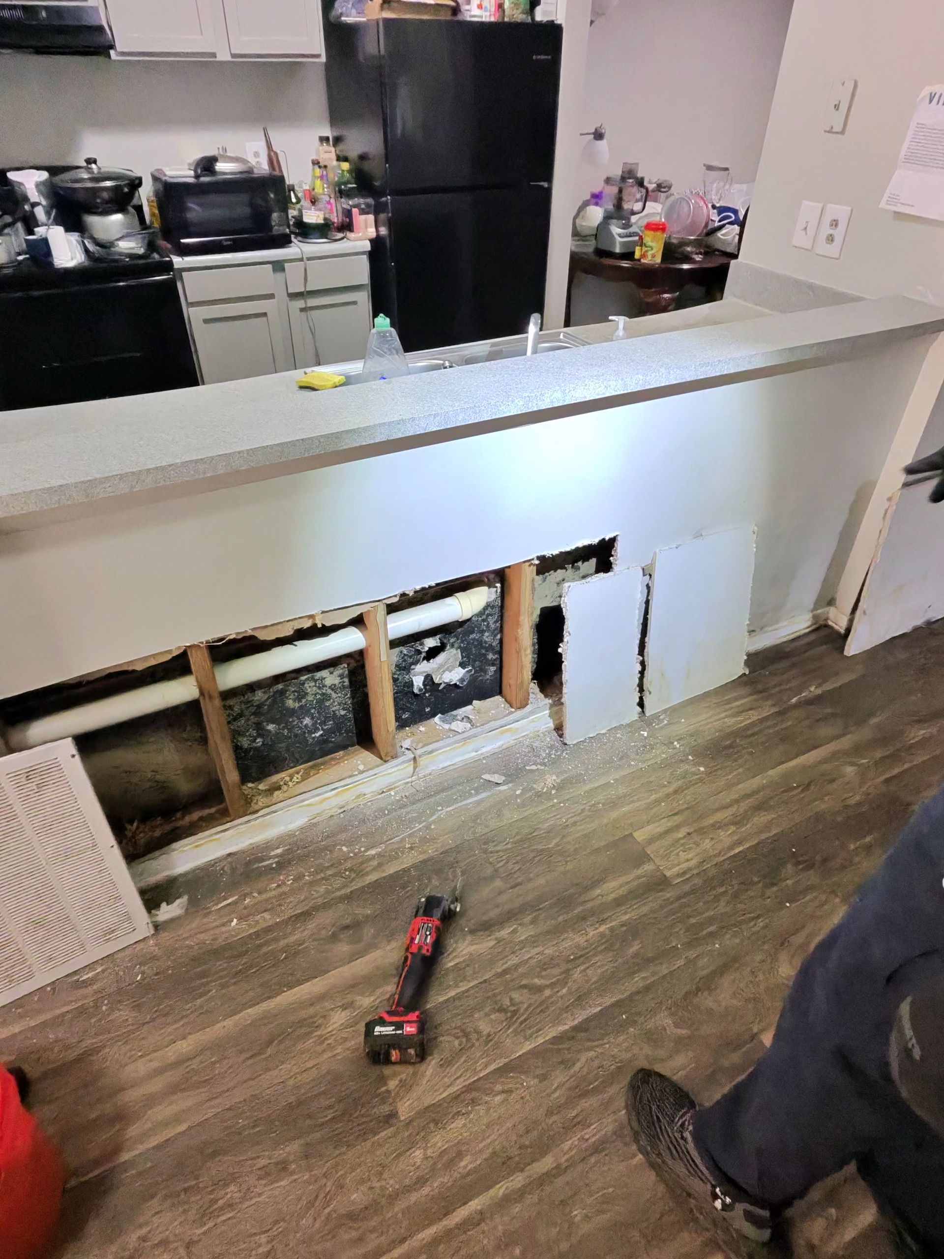 Kitchen renovation, damaged cabinet under counter. Drill on floor, exposed plumbing.