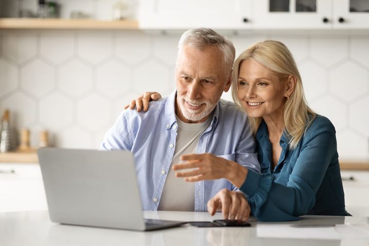 happy senior couple paying bills online with laptop in kitchen