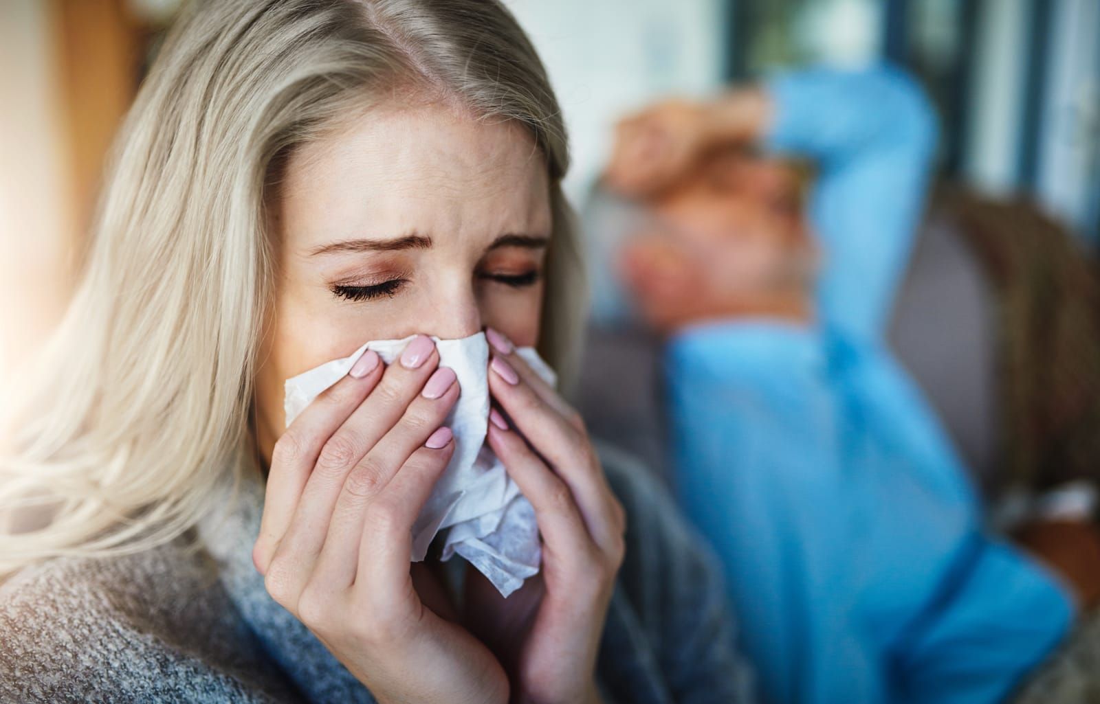 A woman suffering from sinusitis is blowing her nose into a napkin.