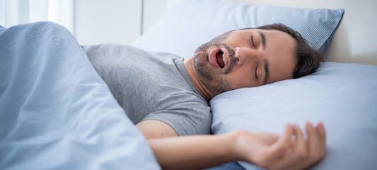 A man is sleeping in a bed with his mouth open.