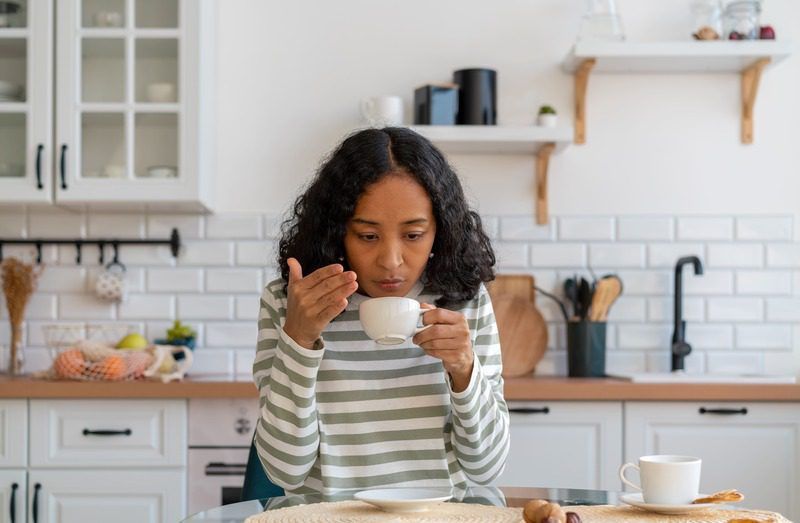 A woman is drinking a cup of coffee in a kitchen.