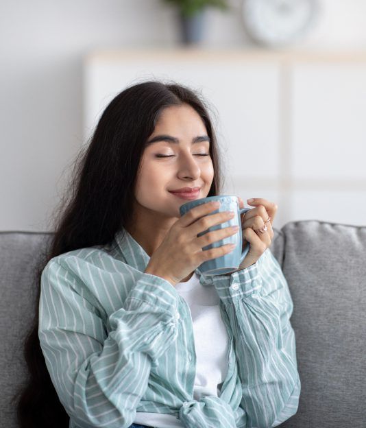 A woman is sitting on a couch drinking a cup of coffee.