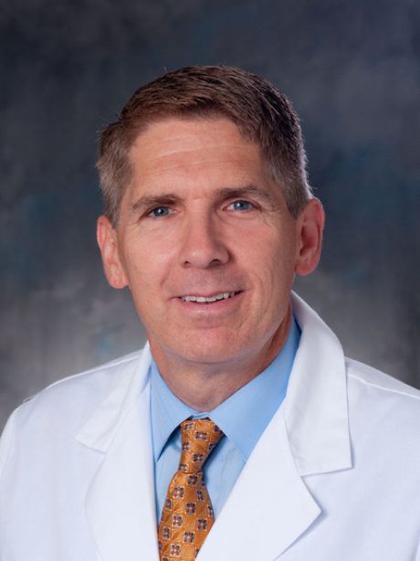 A man in a white coat and tie is smiling for the camera