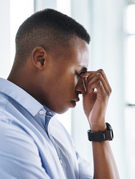 A man in a blue shirt is covering his face with his hand.