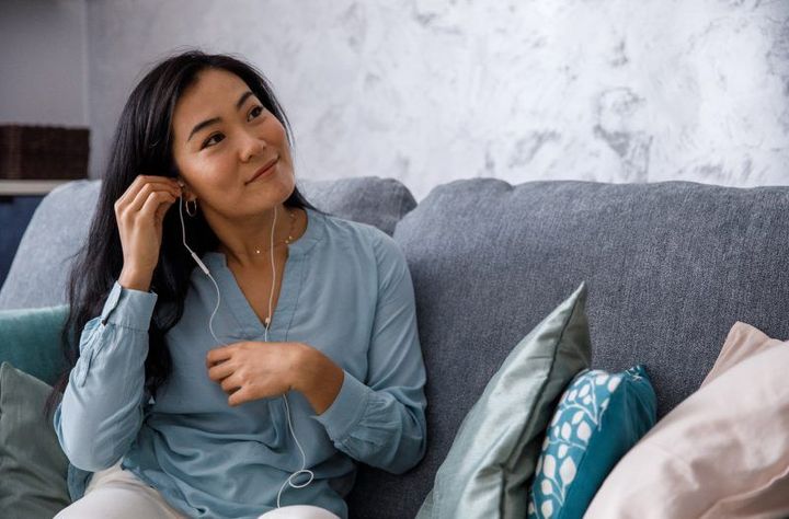 A woman is sitting on a couch listening to music with headphones.