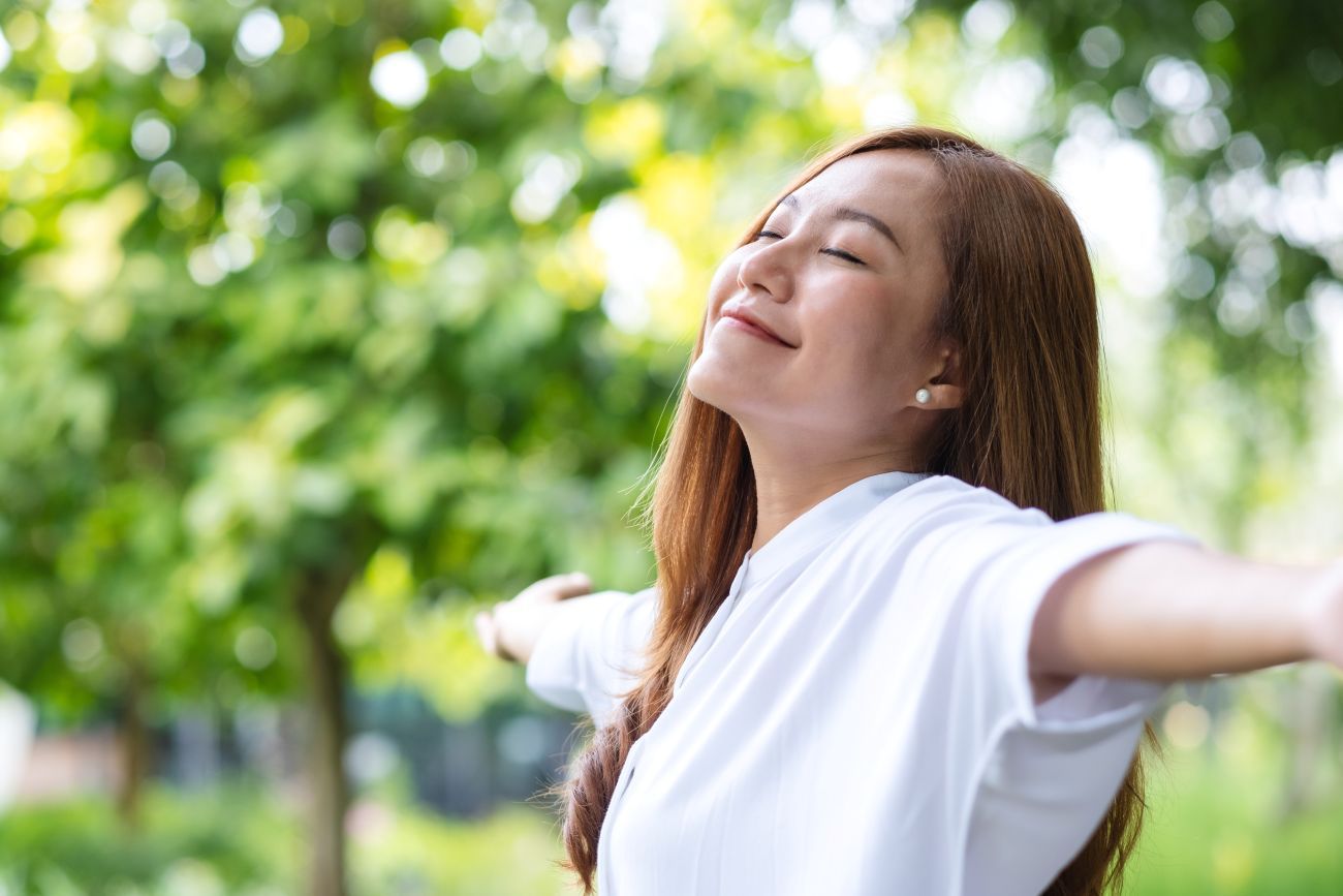 A woman is standing in a park with her arms outstretched.