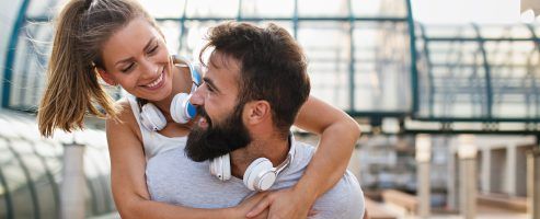 A man is carrying a woman on his back while wearing headphones.