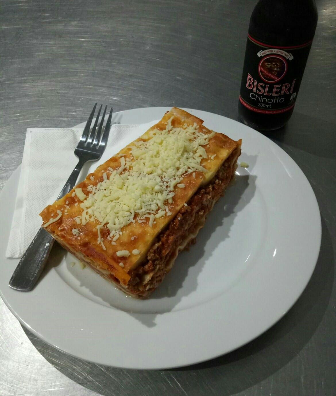 A White Plate Topped With A Lasagna Next To A Bottle Of Bisleri — Bel-Air Pizza In Port Macquarie, NSW