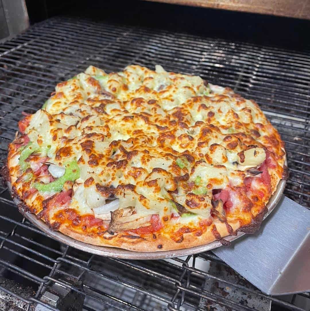 A Pizza Is Being Cooked On A Grill With A Spatula — Bel-Air Pizza In Port Macquarie, NSW