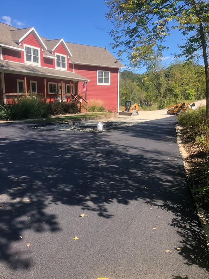 A two-story red building with a porch sits beside a paved driveway on a sunny day with trees in the background.