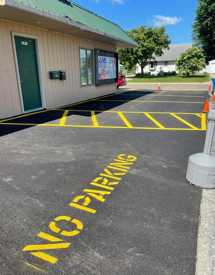 A beige building with a green roof next to an asphalt parking area featuring bright yellow 