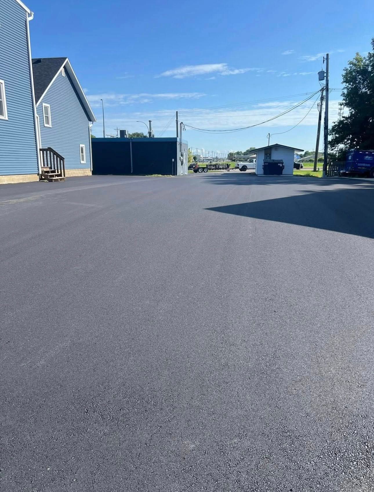 A freshly paved, empty parking lot next to a blue building on a bright, sunny day.