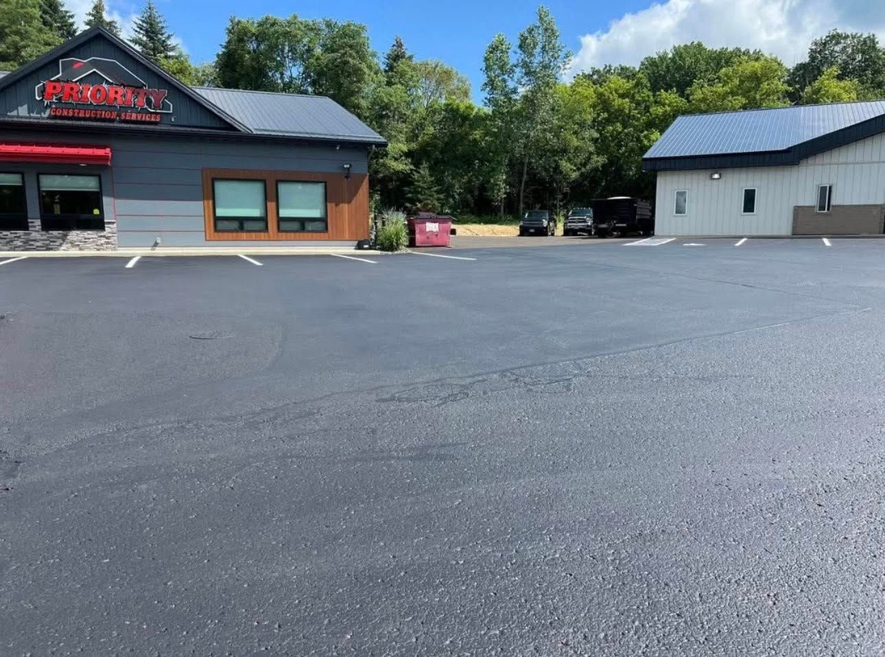 A freshly paved black asphalt parking lot in front of two commercial buildings on a sunny day.