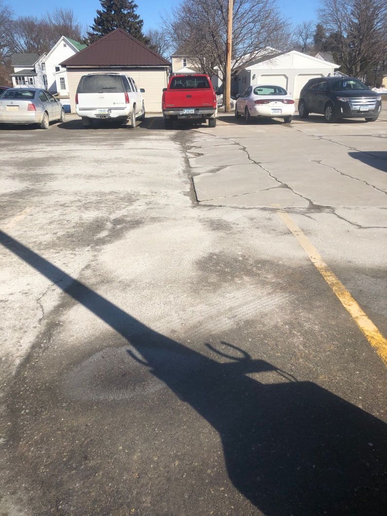 A parking lot featuring a row of parked cars near a building, with a long, dark shadow cast across the foreground.