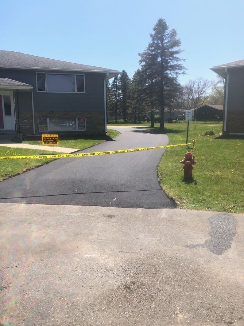 A freshly paved driveway in front of a house, marked off with yellow caution tape, next to a red fire hydrant.
