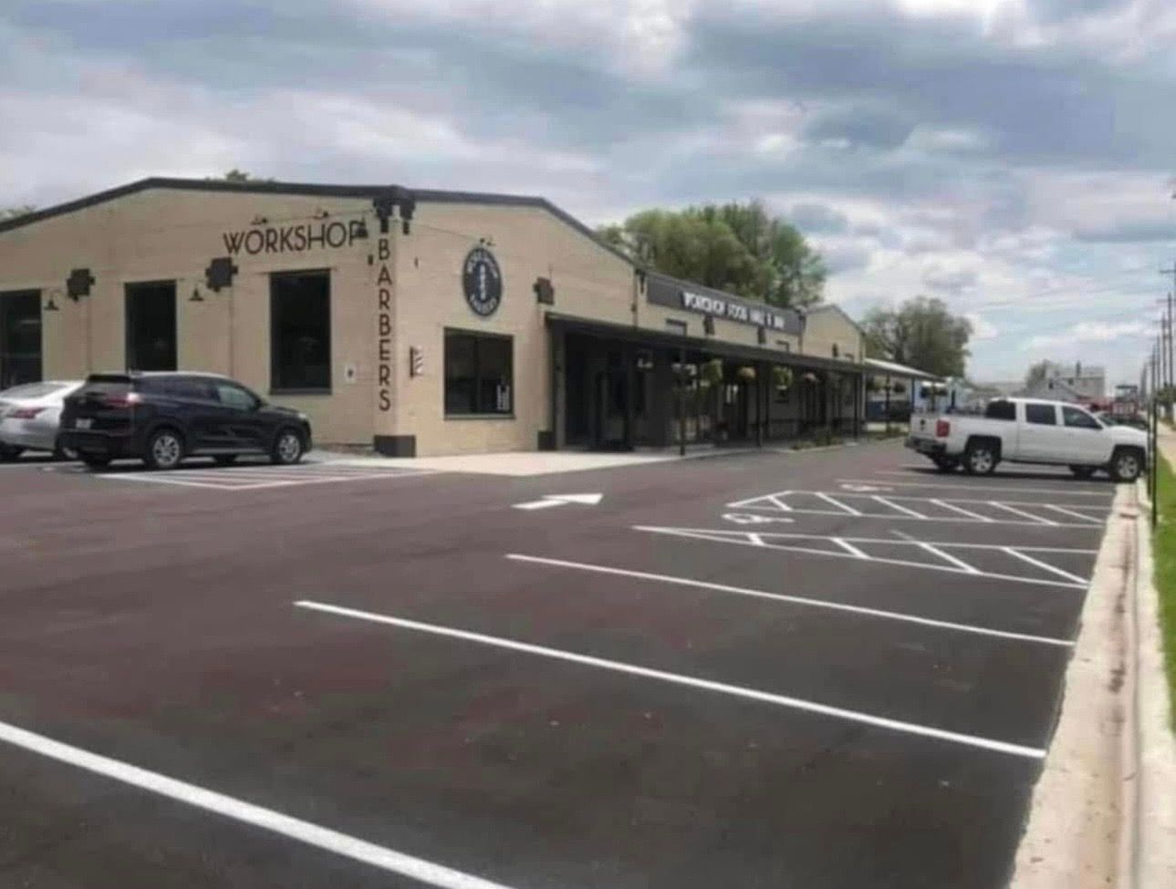 A dark-colored pickup truck towing a trailer with a red logo on a freshly paved parking lot in front of Dave's store.