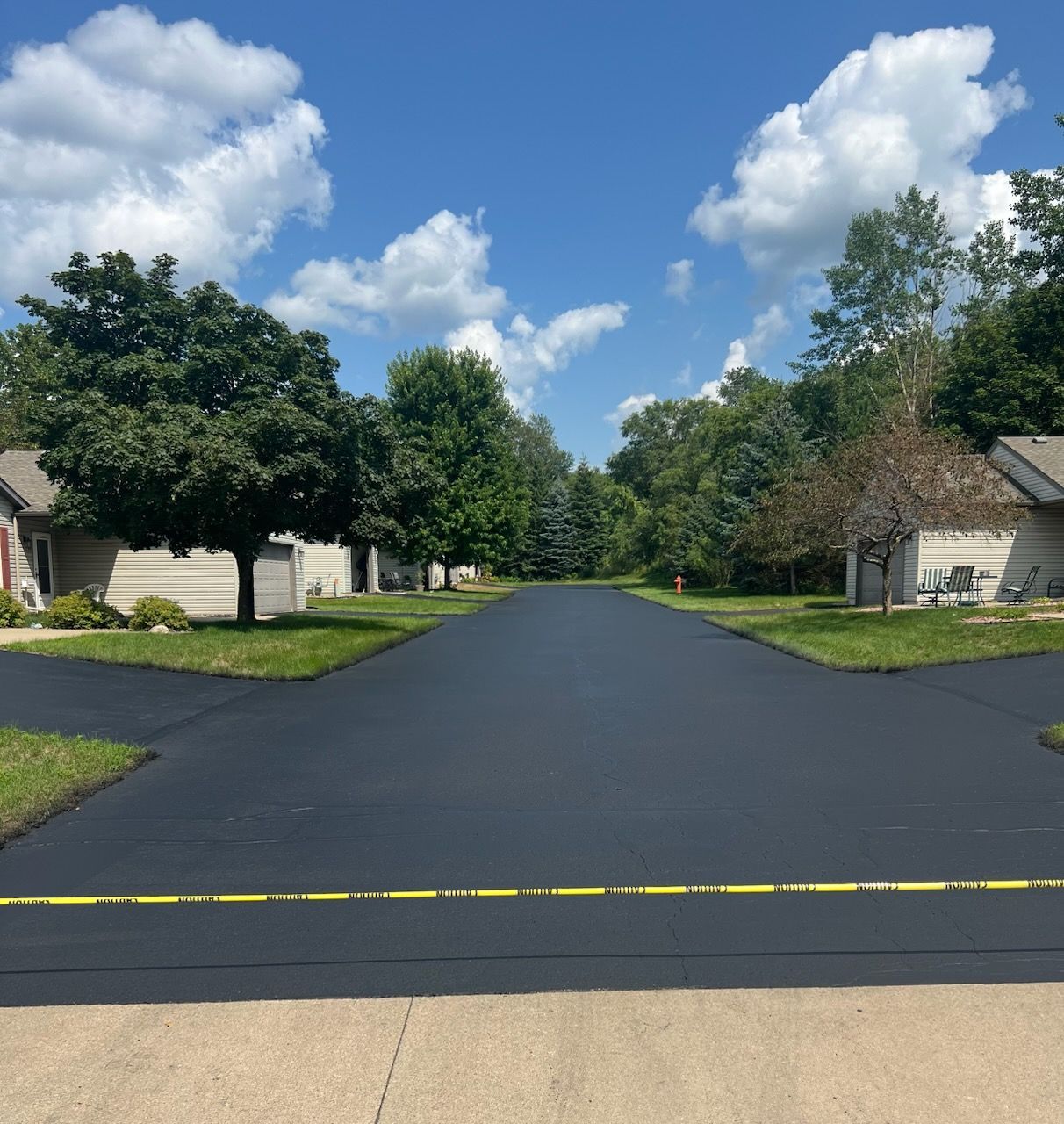 A red dump truck and construction equipment parked near a newly paved asphalt section in a commercial parking lot.