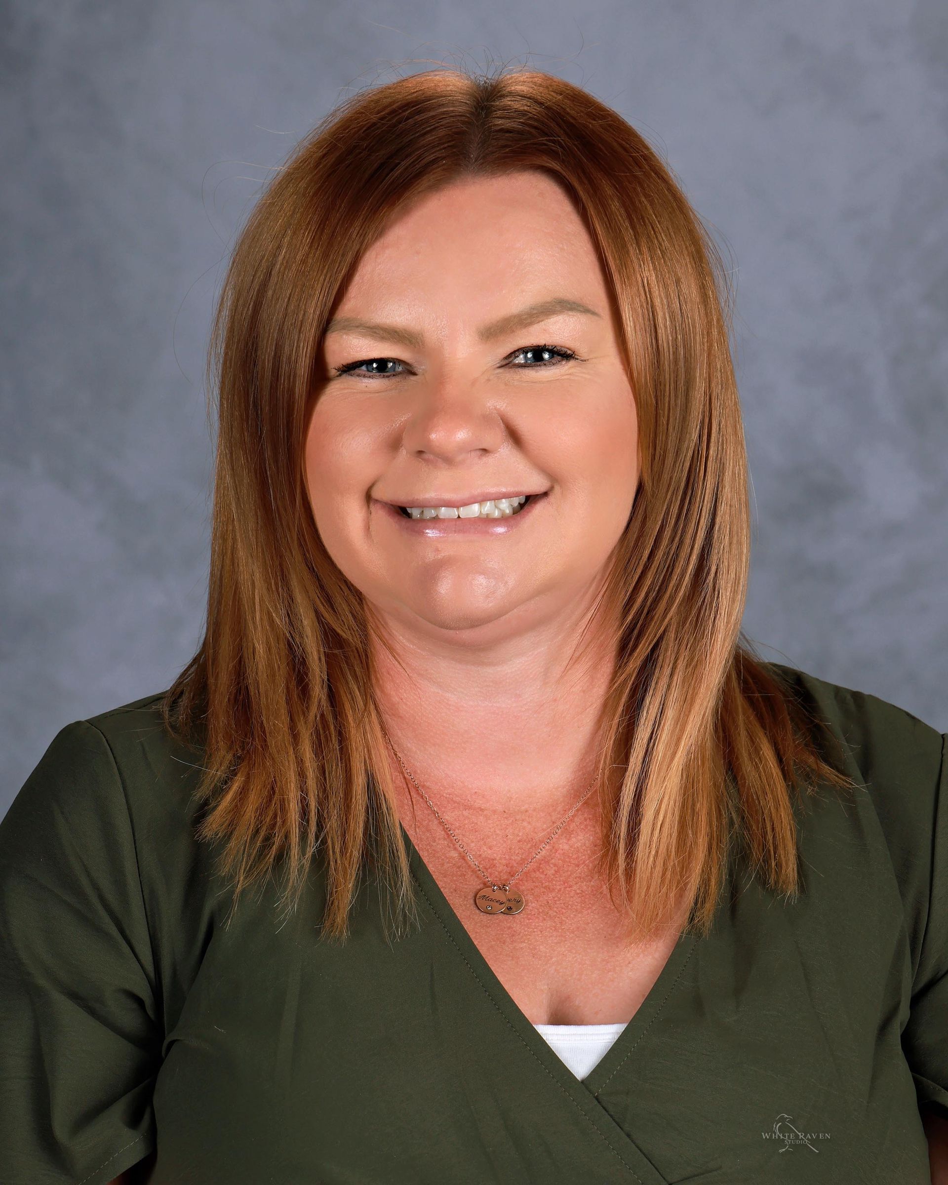 A woman wearing a blue shirt and a necklace is smiling for a picture.