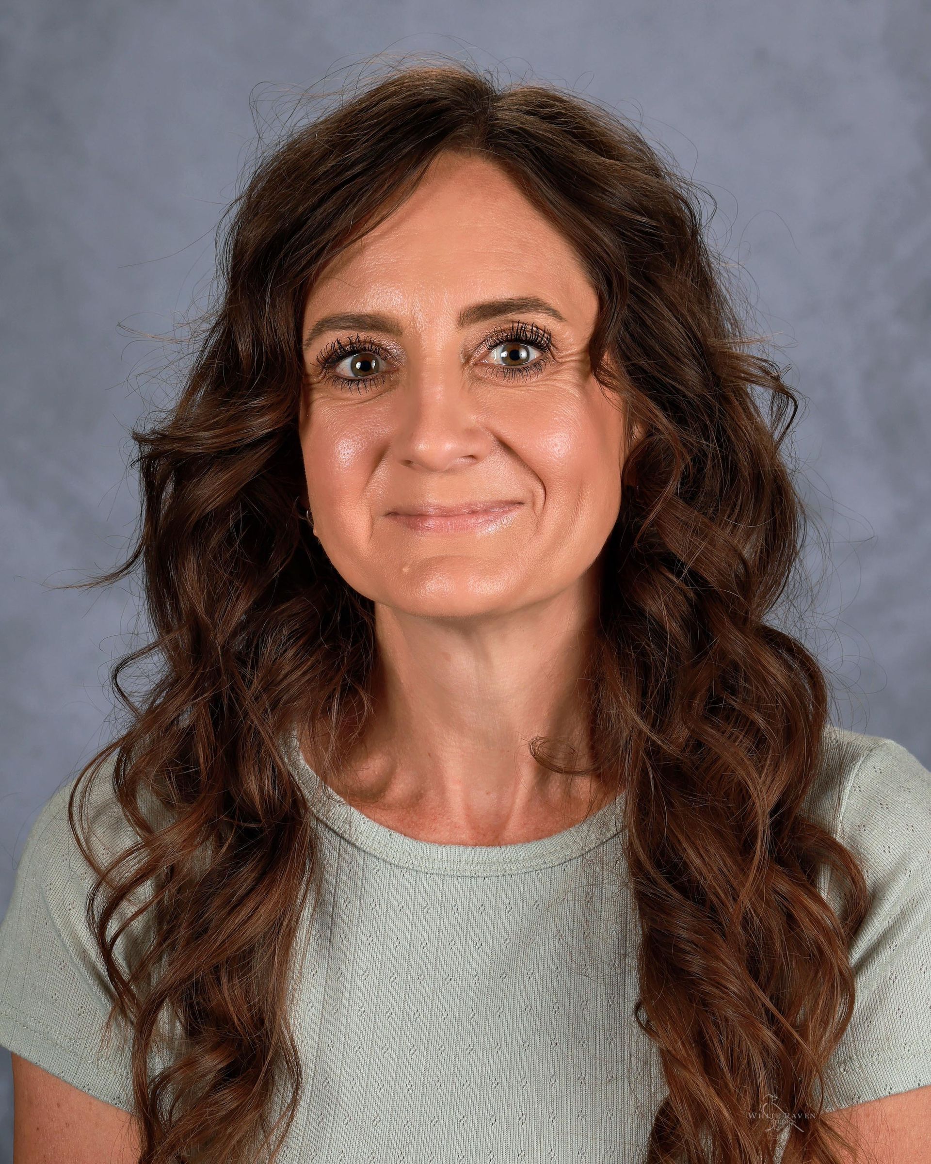 A woman with long hair is wearing a blue shirt and smiling for the camera.