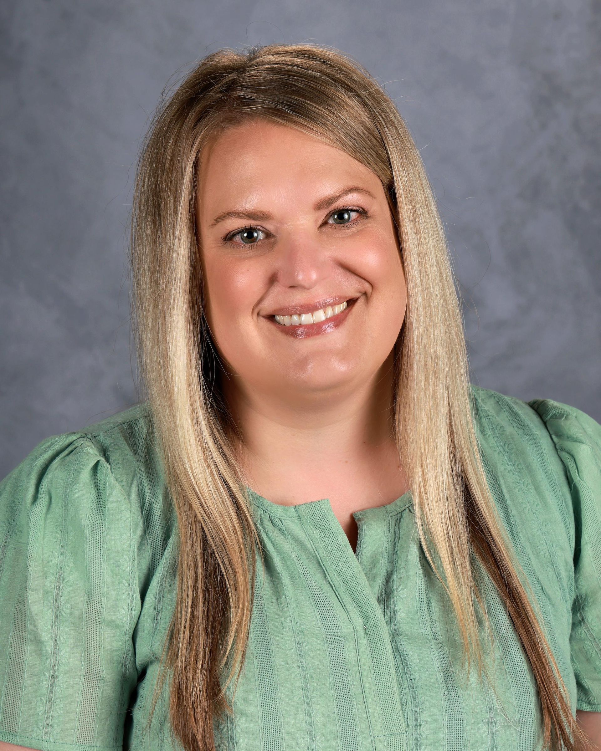 A woman with long brown hair is smiling for a picture.