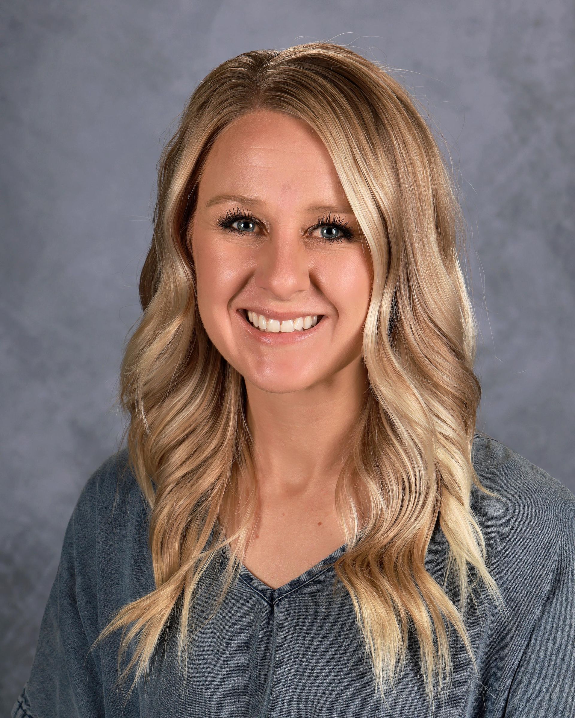 A woman with blonde hair and blue eyes is smiling for a picture.