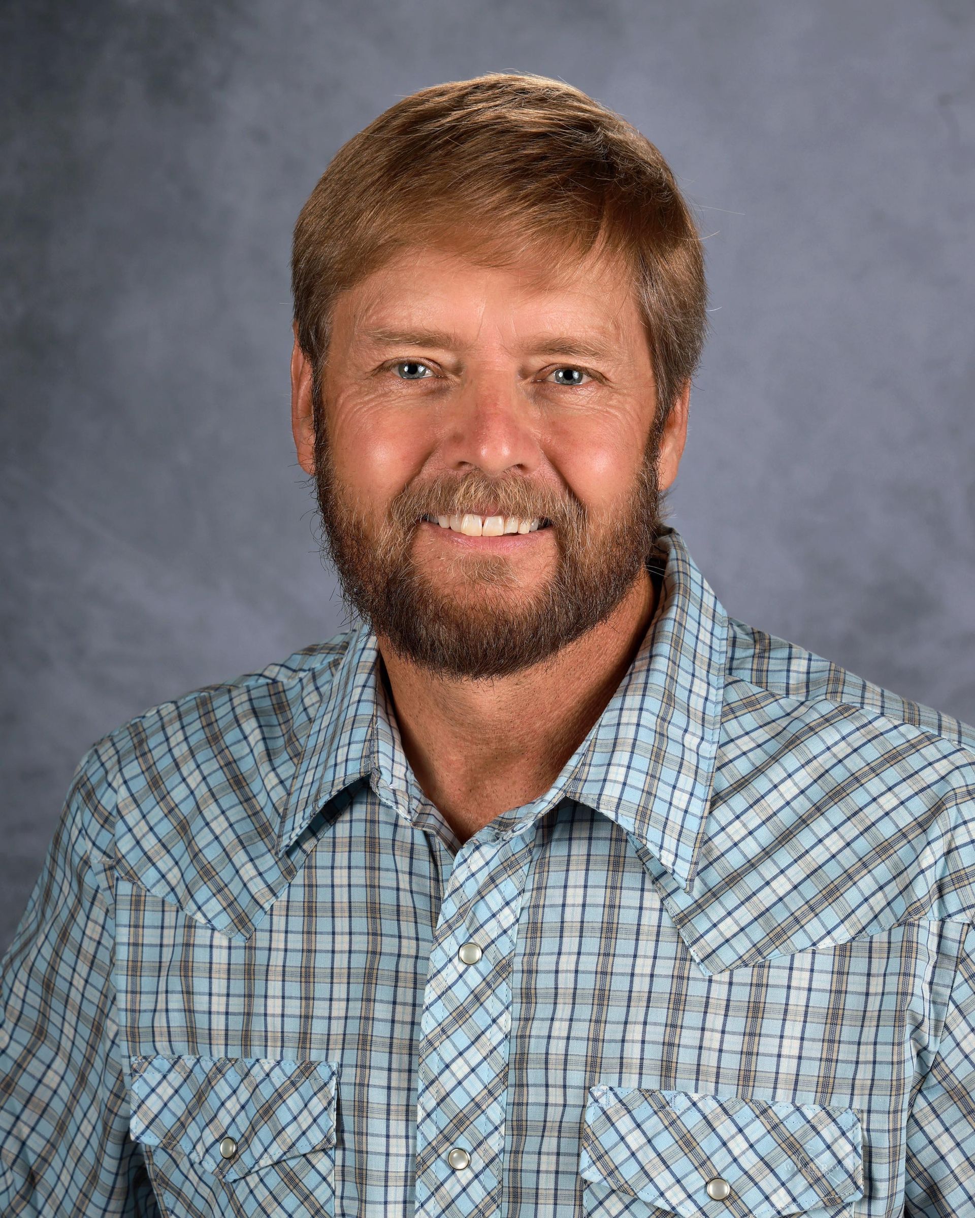 A man with a beard is wearing a plaid shirt and smiling for the camera.