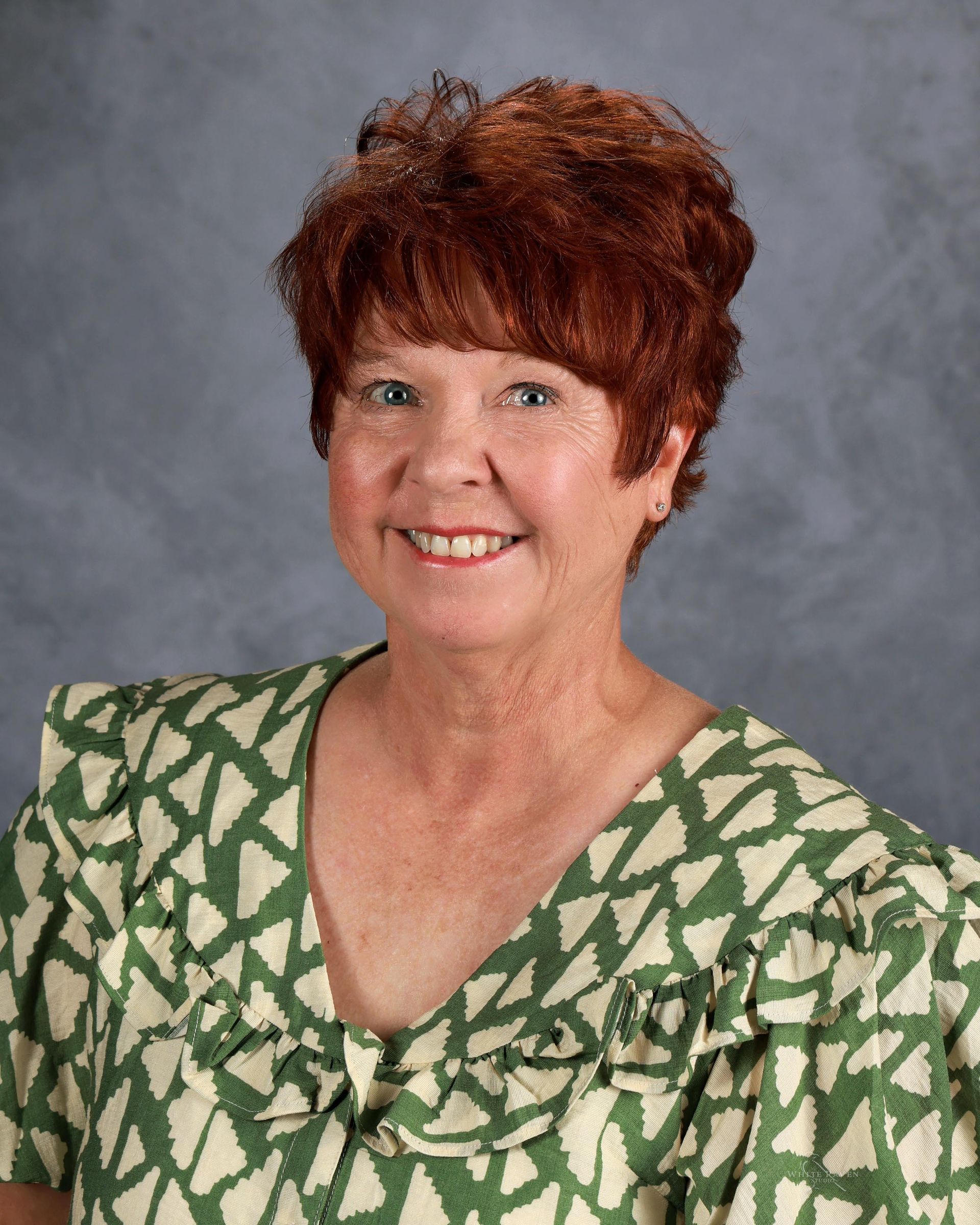 A woman with red hair is wearing a floral shirt and smiling for the camera.