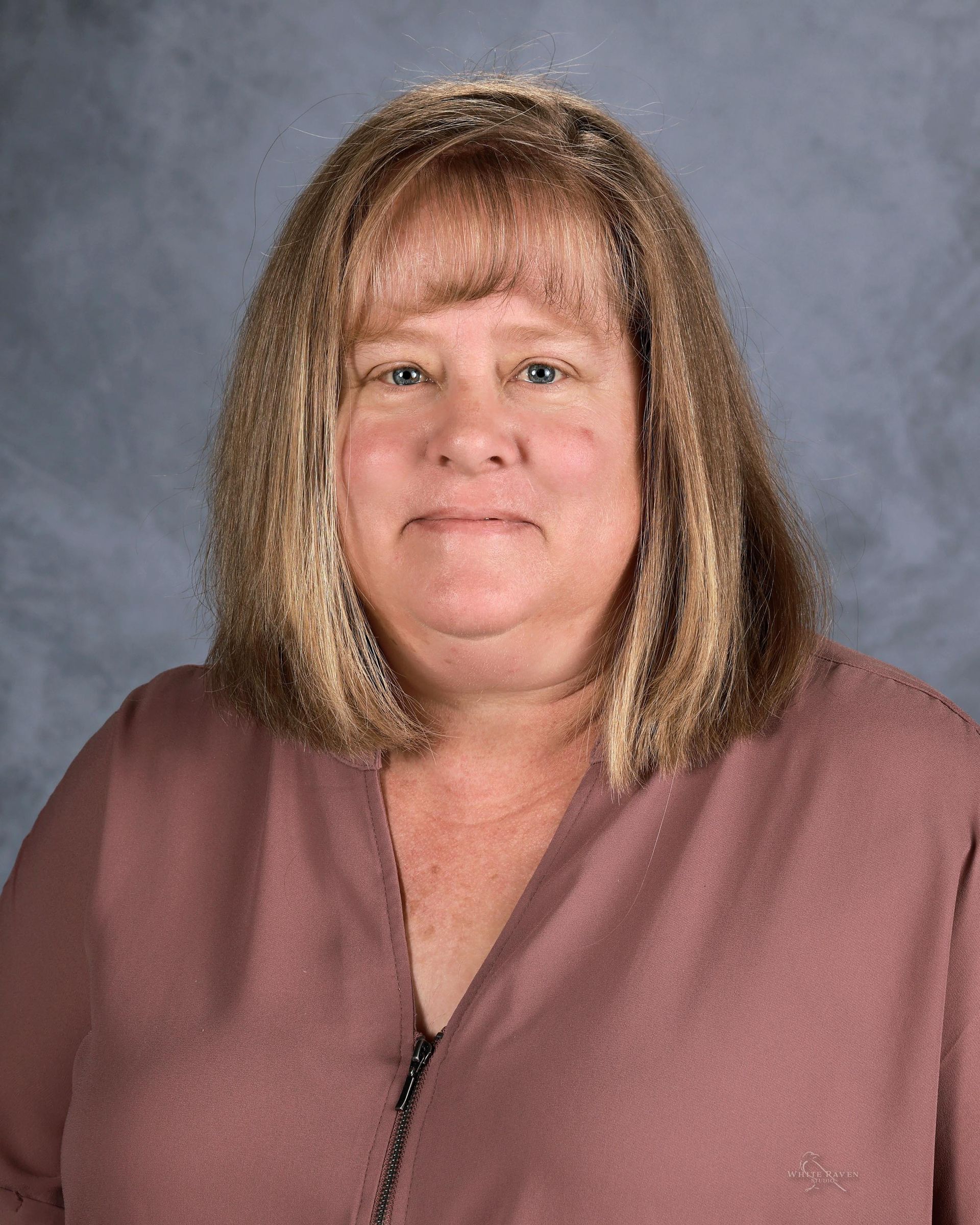A woman with long blonde hair is wearing a blue shirt and smiling for the camera.