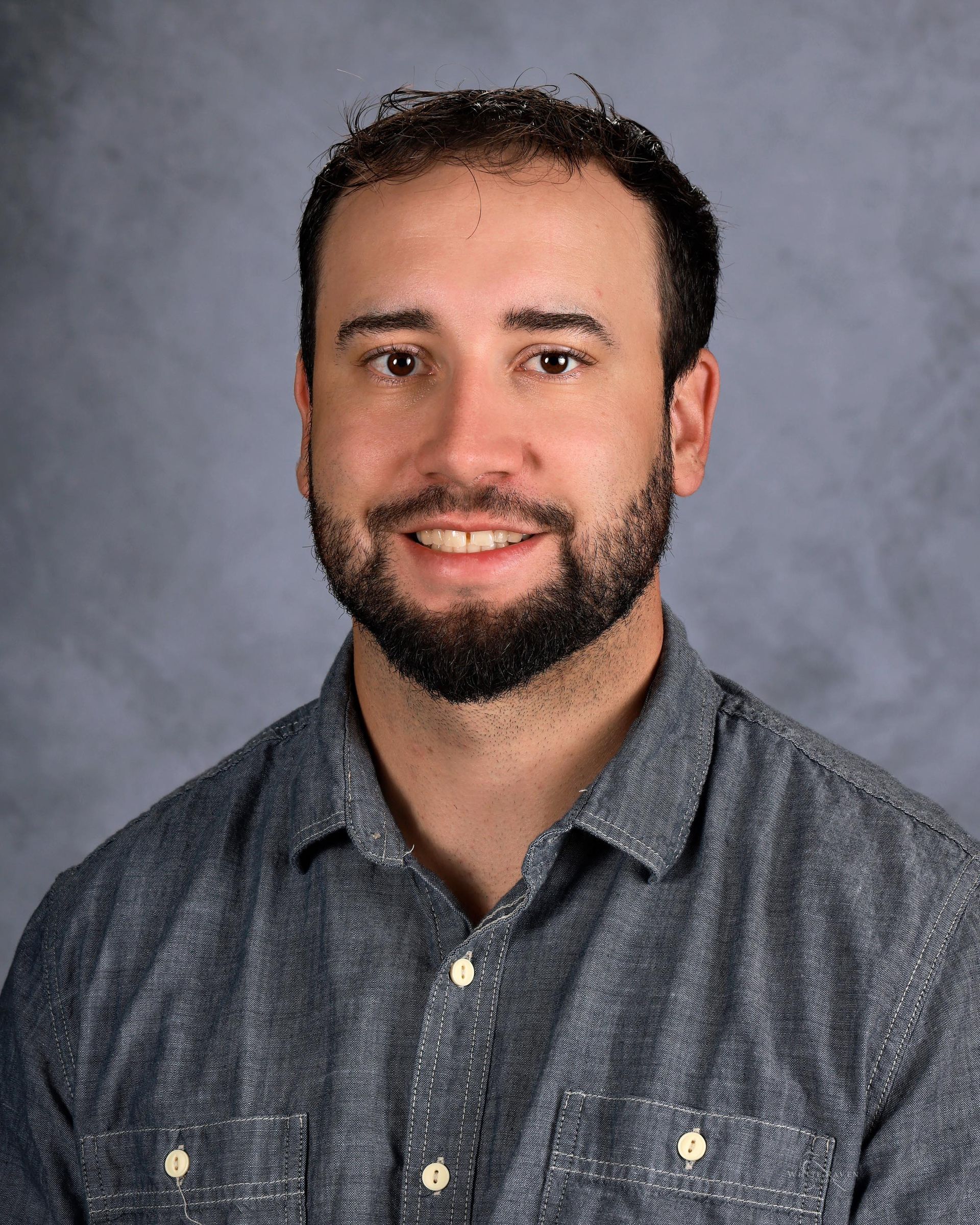 A man with a beard wearing a plaid shirt is smiling for the camera