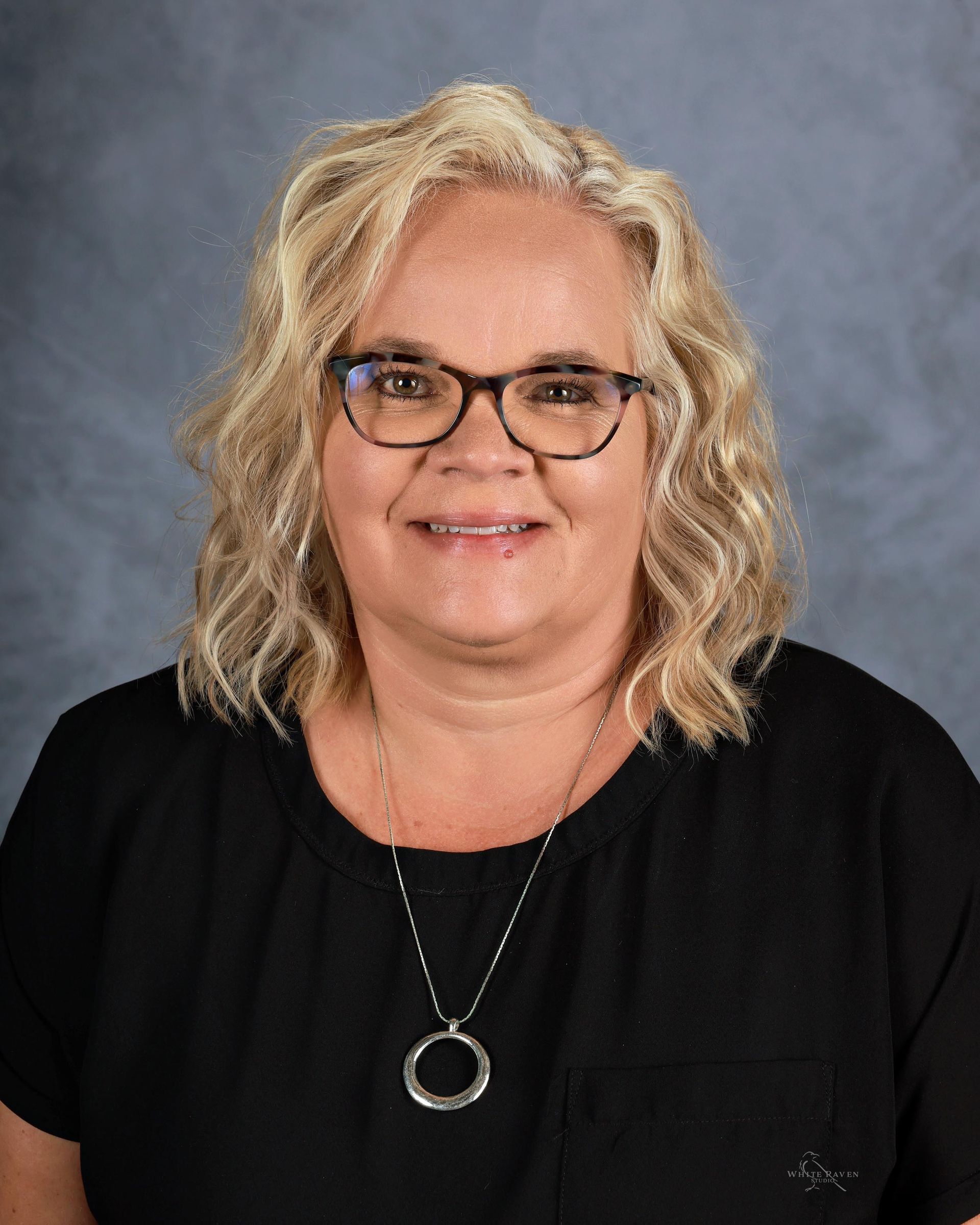 A woman wearing glasses and a green shirt is smiling for a picture.