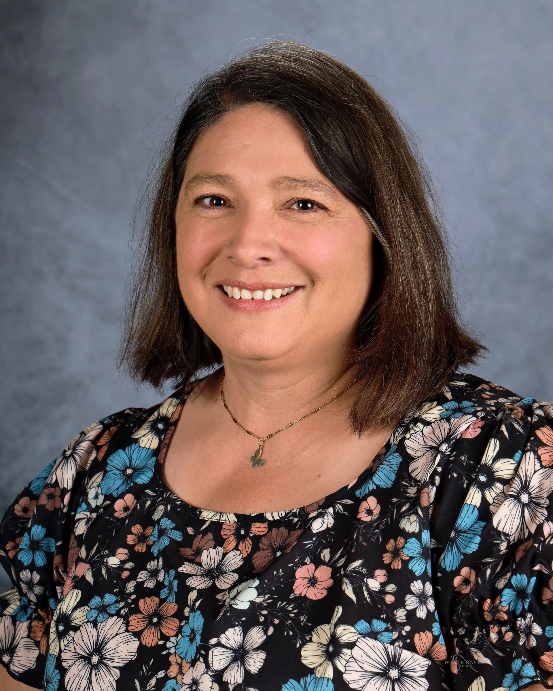 A woman in a blue shirt and necklace is smiling for the camera.