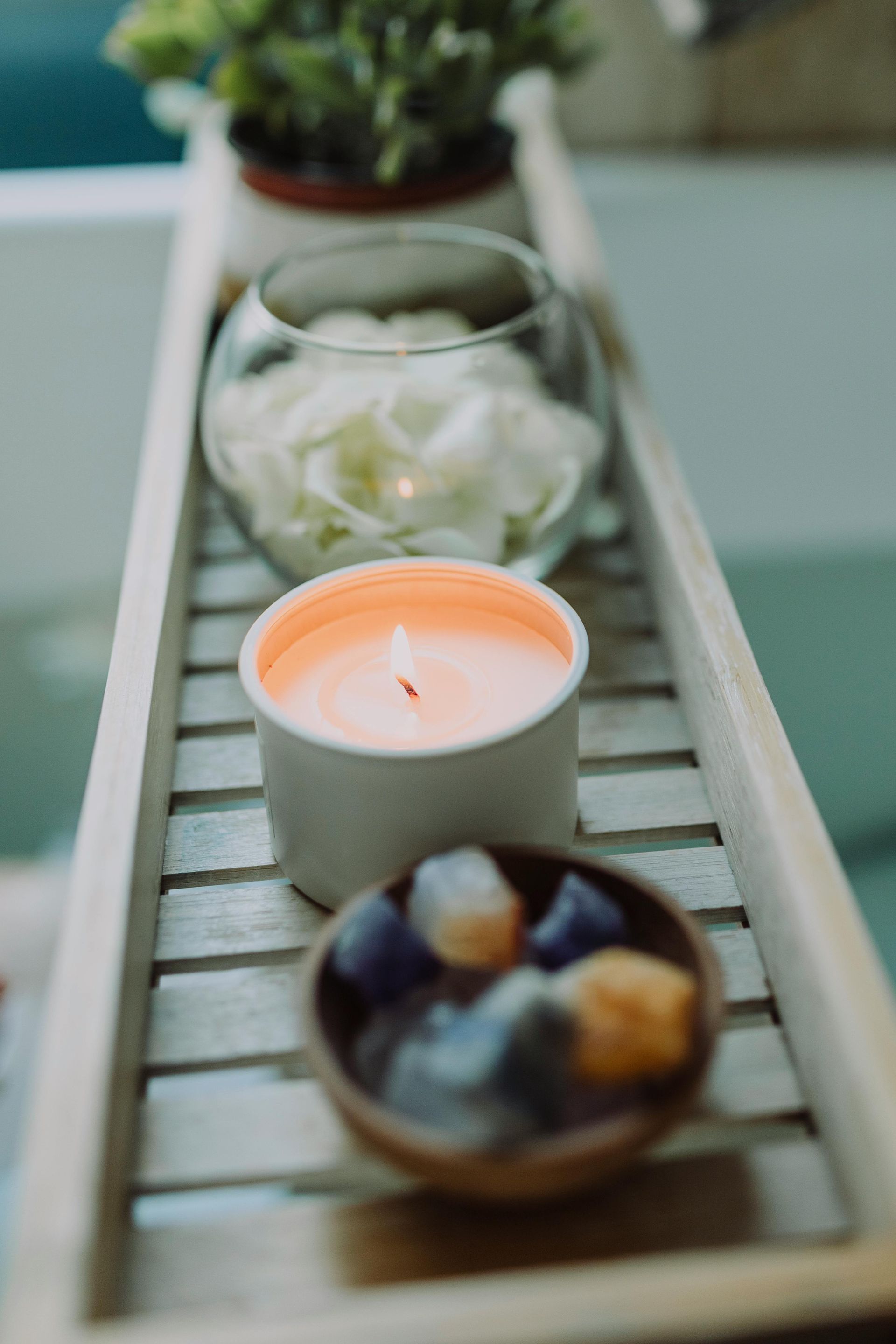 Houten dienblad met een brandende kaars, een schaal met kristallen en een glazen vaas met bloemblaadjes.