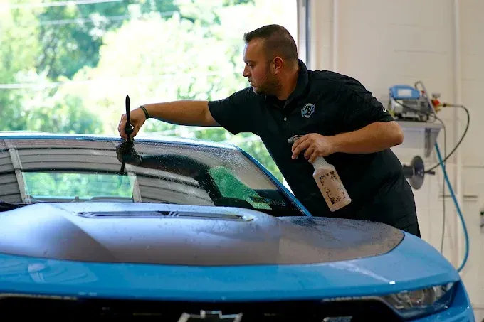 Technician applying auto window tint to a car's rear windshield using a squeegee and spray solution