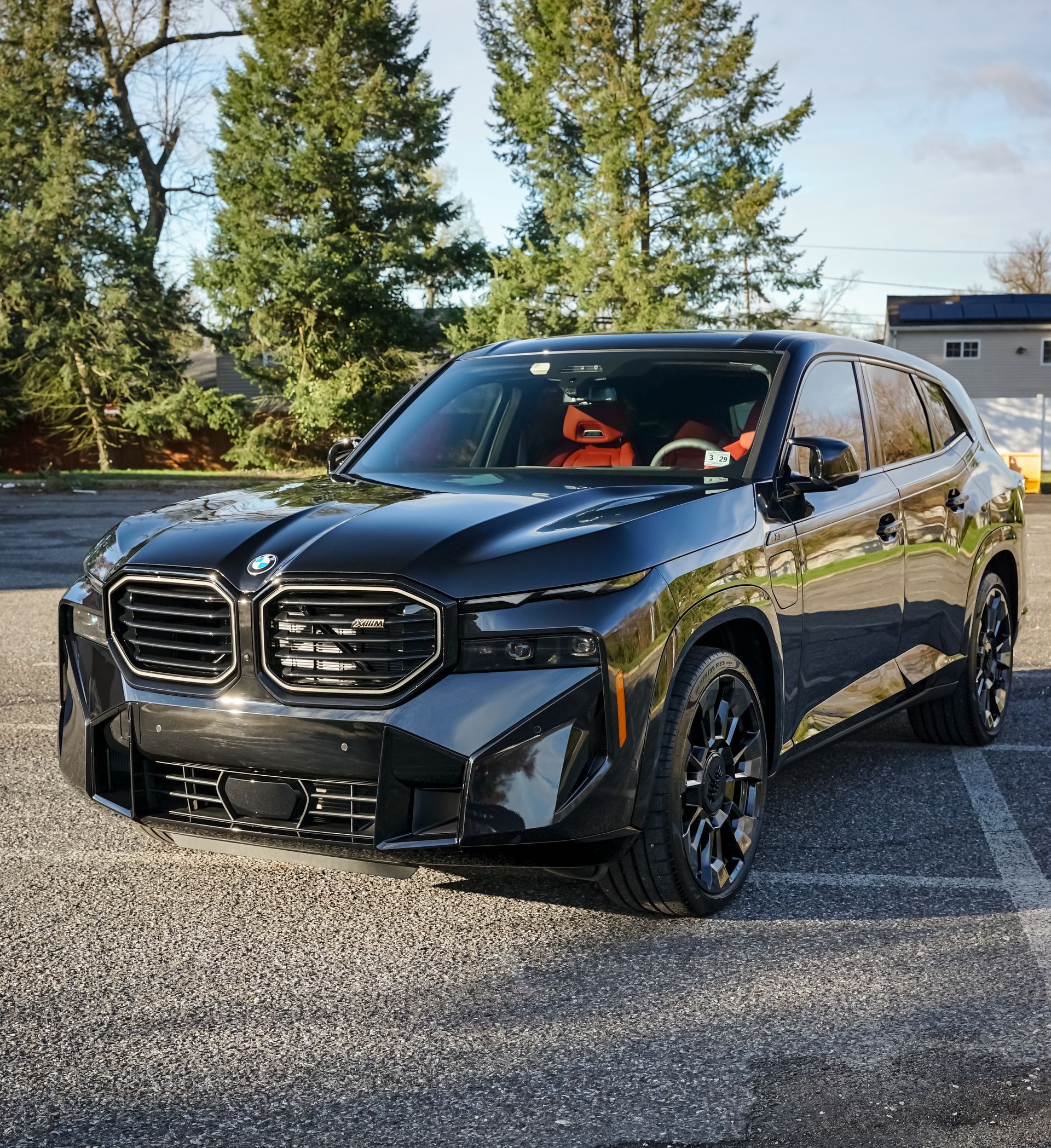 A black car is parked in a parking lot with trees in the background.