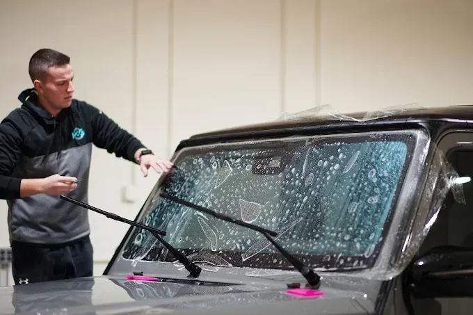Technician installing auto window tint on a car's windshield with suction cup tools holding the glass 