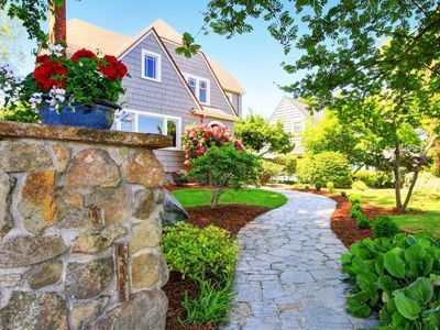 A stone walkway leading to a house with a stone wall.