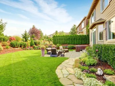 A lush green backyard with a stone walkway leading to a patio with a table and chairs.