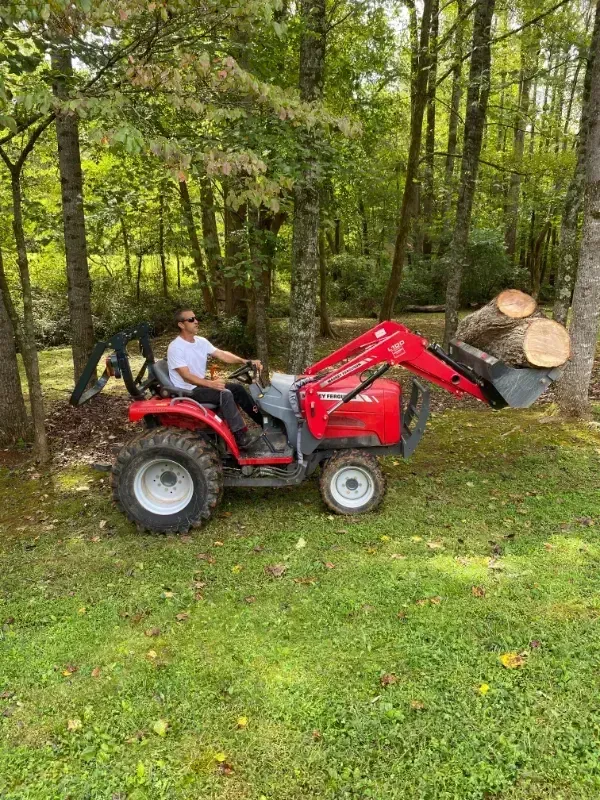 A man is driving a tractor with a bucket full of logs.