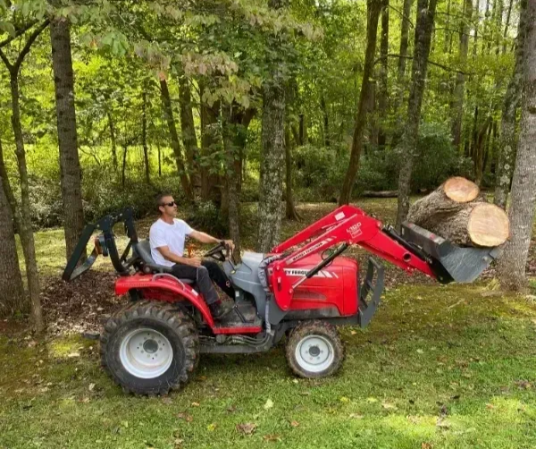 Man operating a red tractor with removed trees in Creedmoor NC.