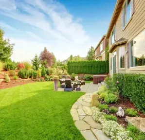 A gray house with black shutters, a stone retaining wall, and a grassy lawn with a person in the background.